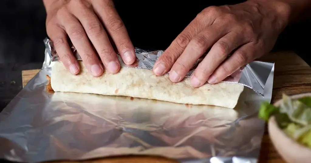 Mężczyzna zwija tortillę na folii aluminiowej