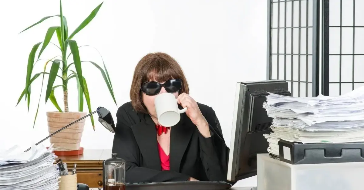 Kobieta w ciemnych okularach ma kaca w pracy.
