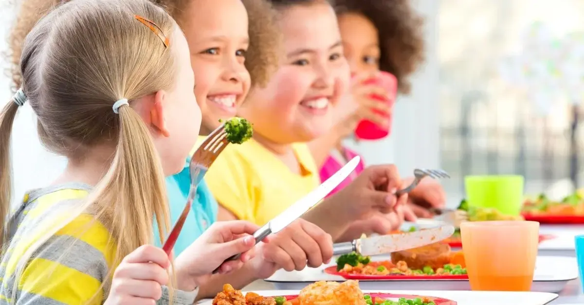 kolacja dla dzieci uśmiechnięte dzieci przy stole jedza