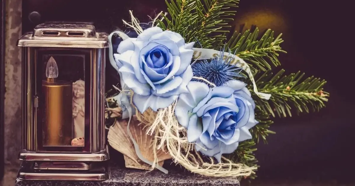 Niebieskie róże i znicz elektroniczny na cmentarzu na Wszystkich Świętych.