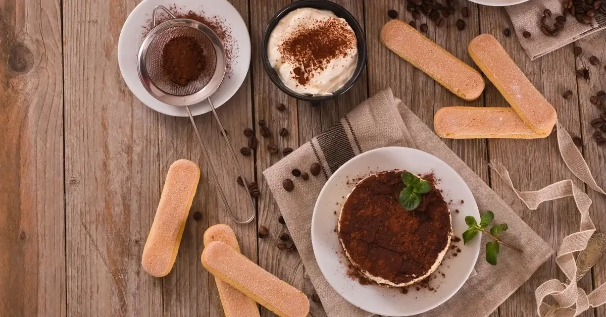 Tiramisu na talerzyku i obok składniki: biszkopty, kakao, krem mascarpone w miseczce