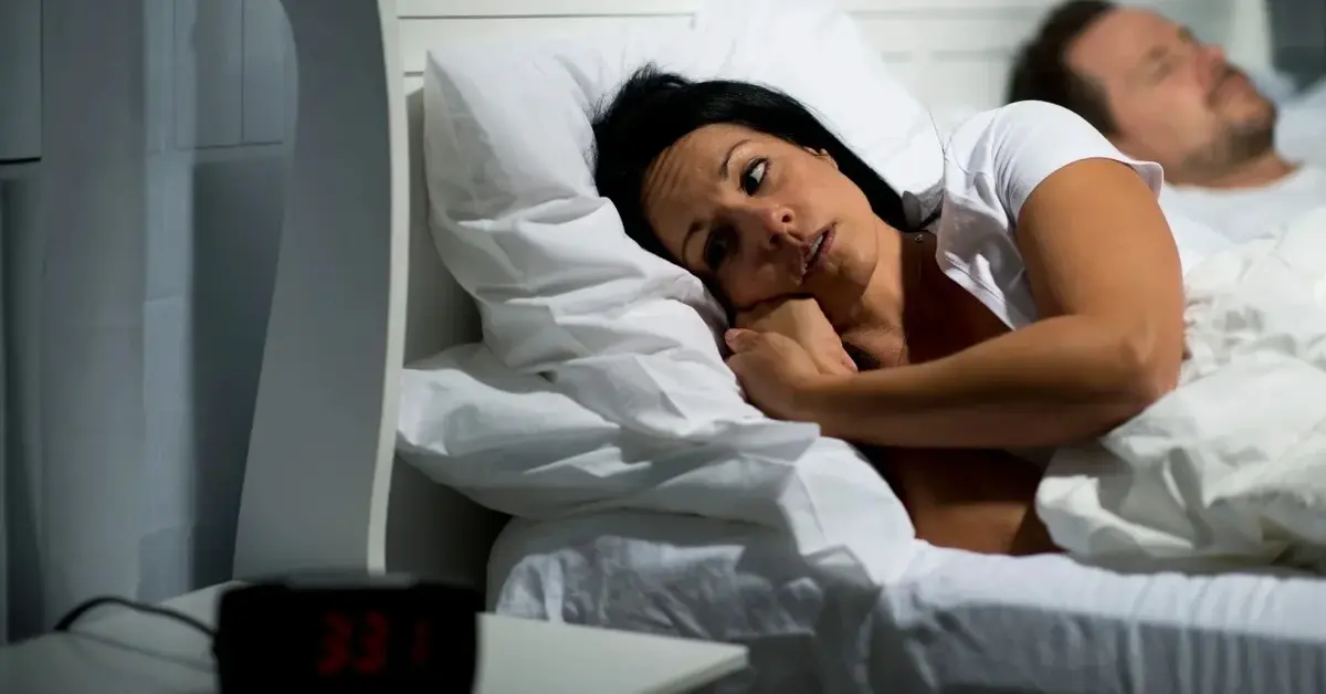 Kobieta leżąca w łóżku, obok śpiący mężczyzna
