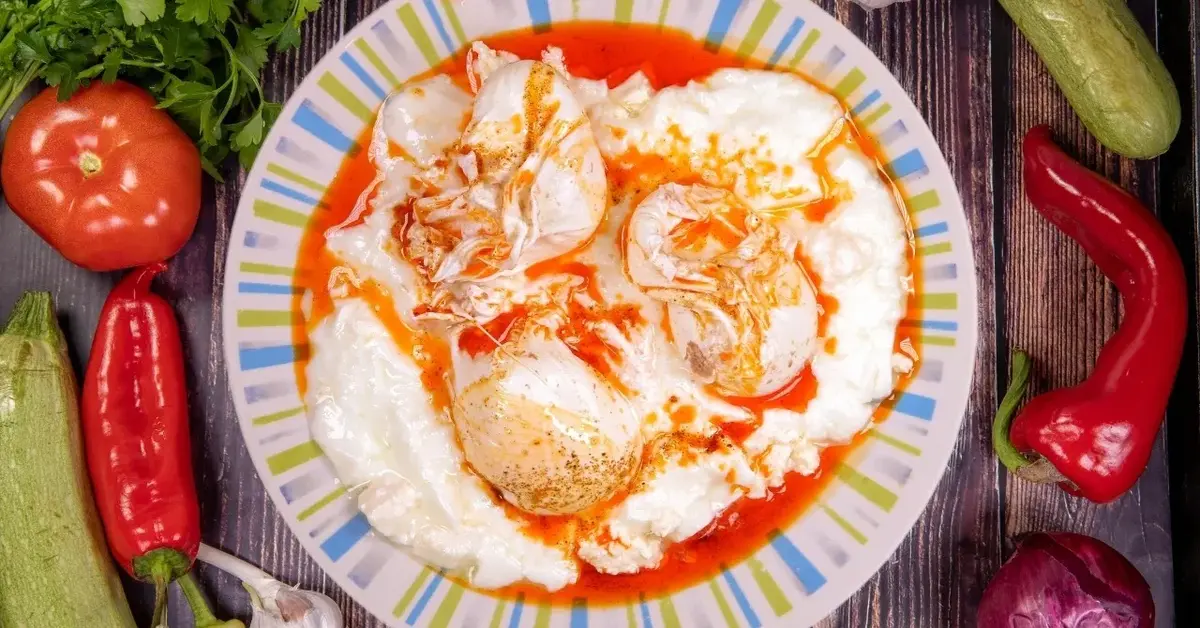 Jajka po turecku z jogurtem na kolorowym talerzu. Dookoła warzywa