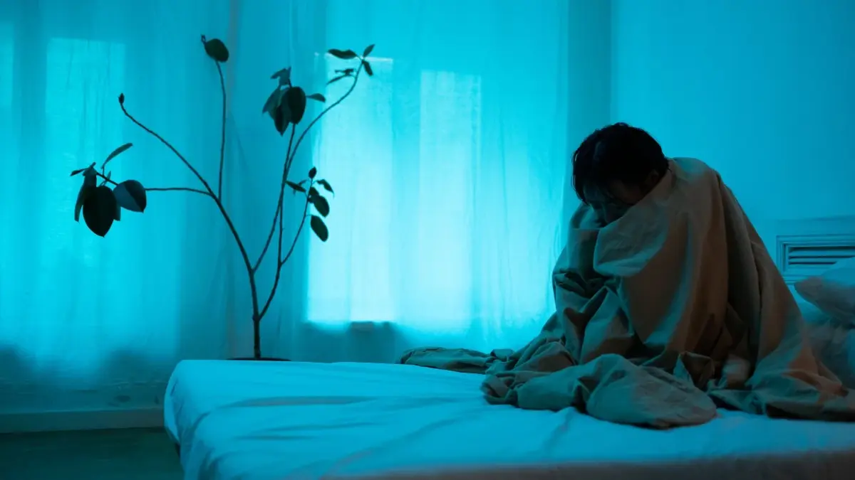 Kobieta otulona kołdra siedząca na łóżku w ciemnym pokoju