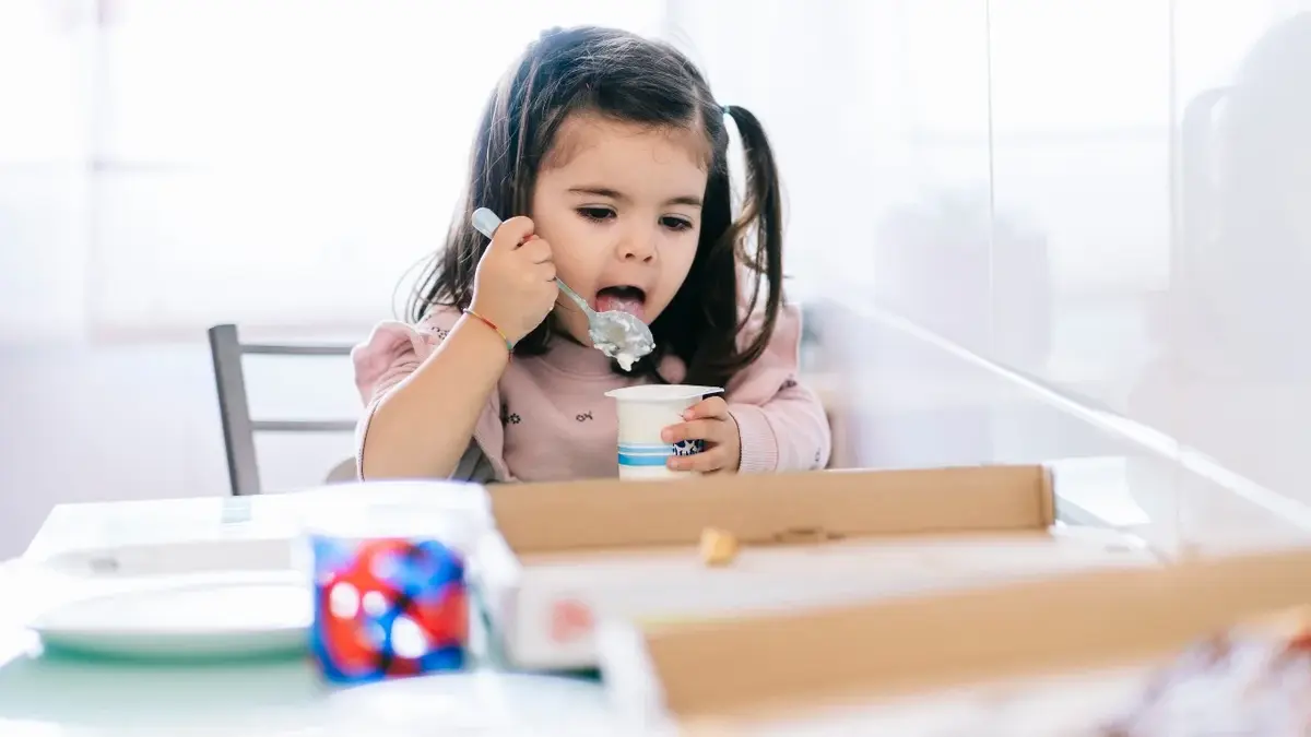 Dziewczynka siedząca przy stole jedząca jogurt łyżeczka 