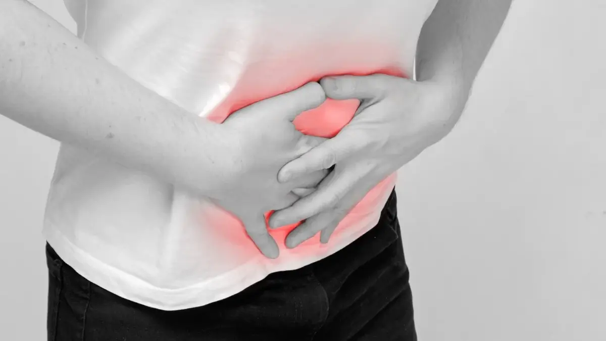 Osoba trzymająca się za brzuch z nałożoną czerwoną grafiką sugerująca ból brzucha