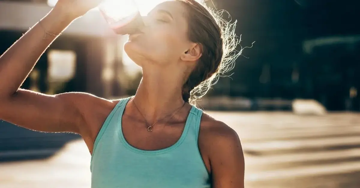 Kobieta w sportowym stroju piję wodę w trakcie upału.