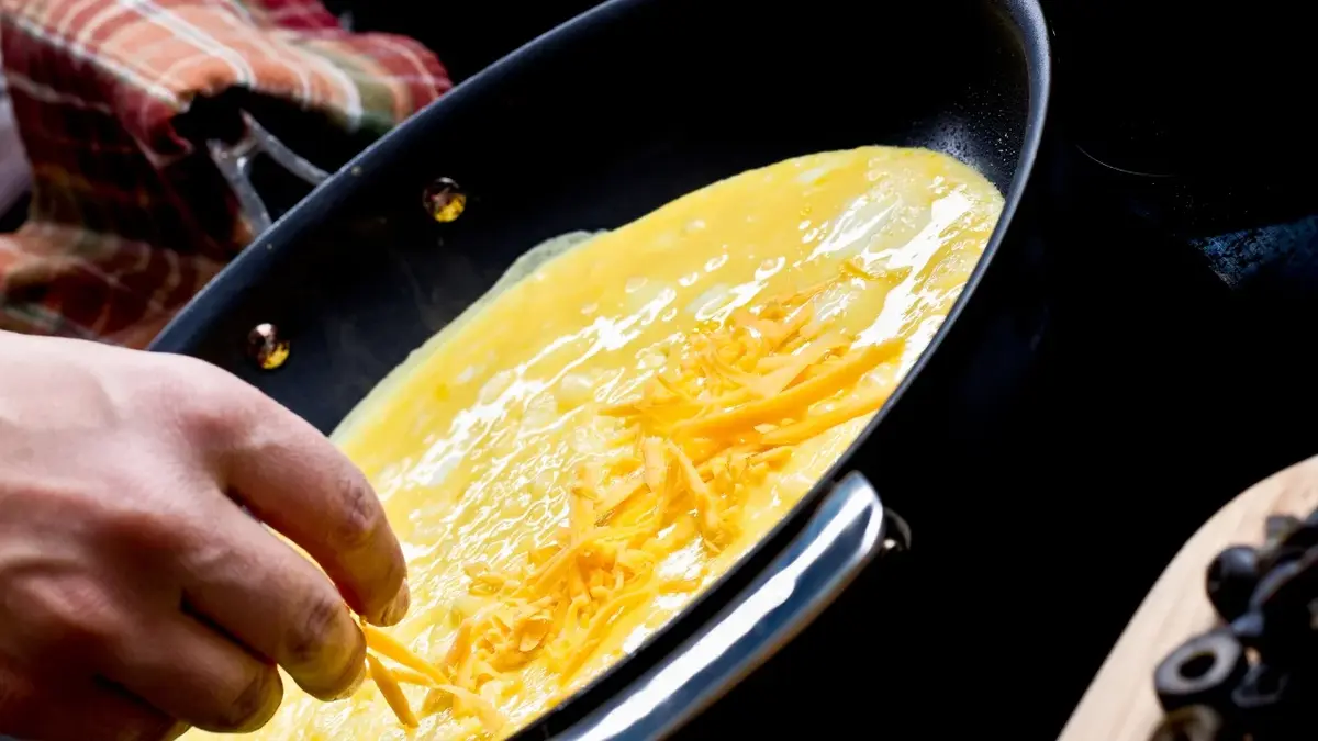 Człowiek posypuje omlet na patelni serem.