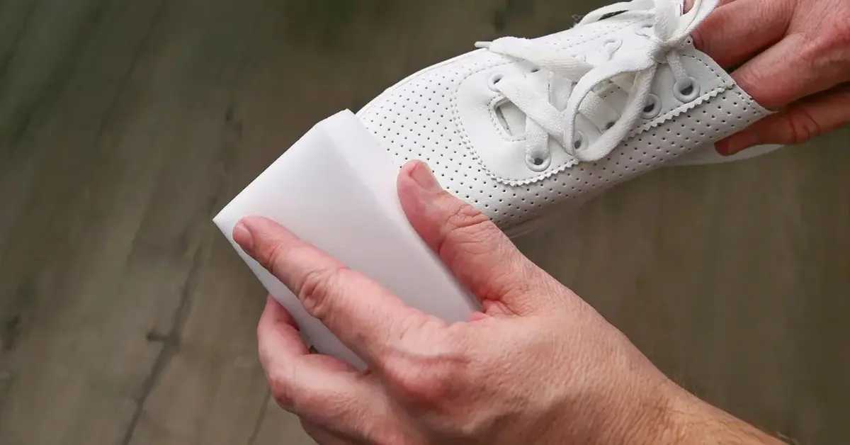 dłoń czyści buty białą magiczną gąbką