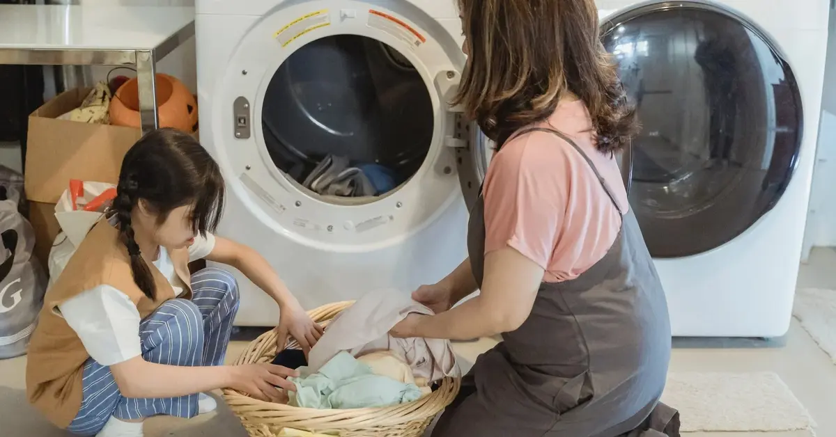 Dziewczynka i kobieta wrzucają pranie do pralki