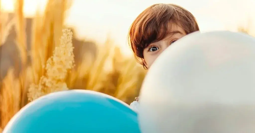 Mały chłopiec wyglądający zza białych i nieieskich balonów