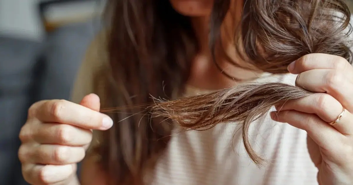 Kobieta z długimi włosami chwyta palcami wypadające włosy