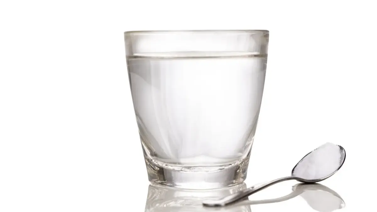 Szklanka wody z elektrolikami, obok łyżeczka z proszkiem