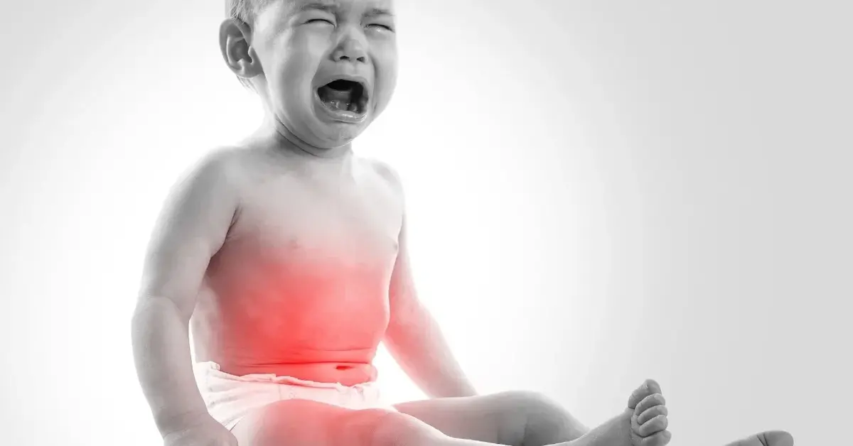 Czarno-białe zdjęcie płaczącego dziecka z zaznaczonym na czerwono obszarem brzuszka