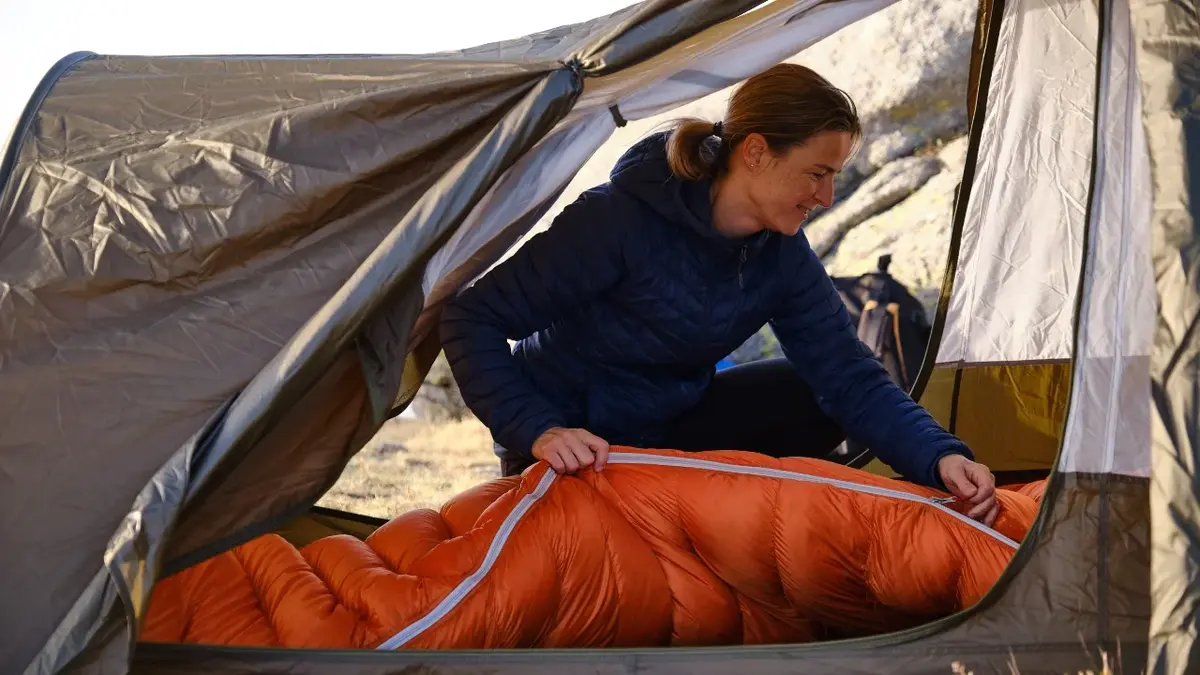 Kobieta zapinająca śpiwór w namiocie 