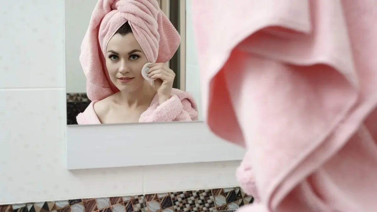Kobieta z różowym ręcznikiem na głowie przeglądająca się lustrze 