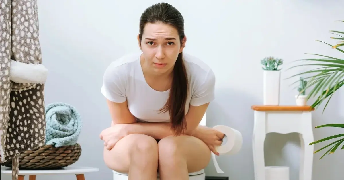 Kobieta siedząca na toalecie i trzymająca się za brzuch 