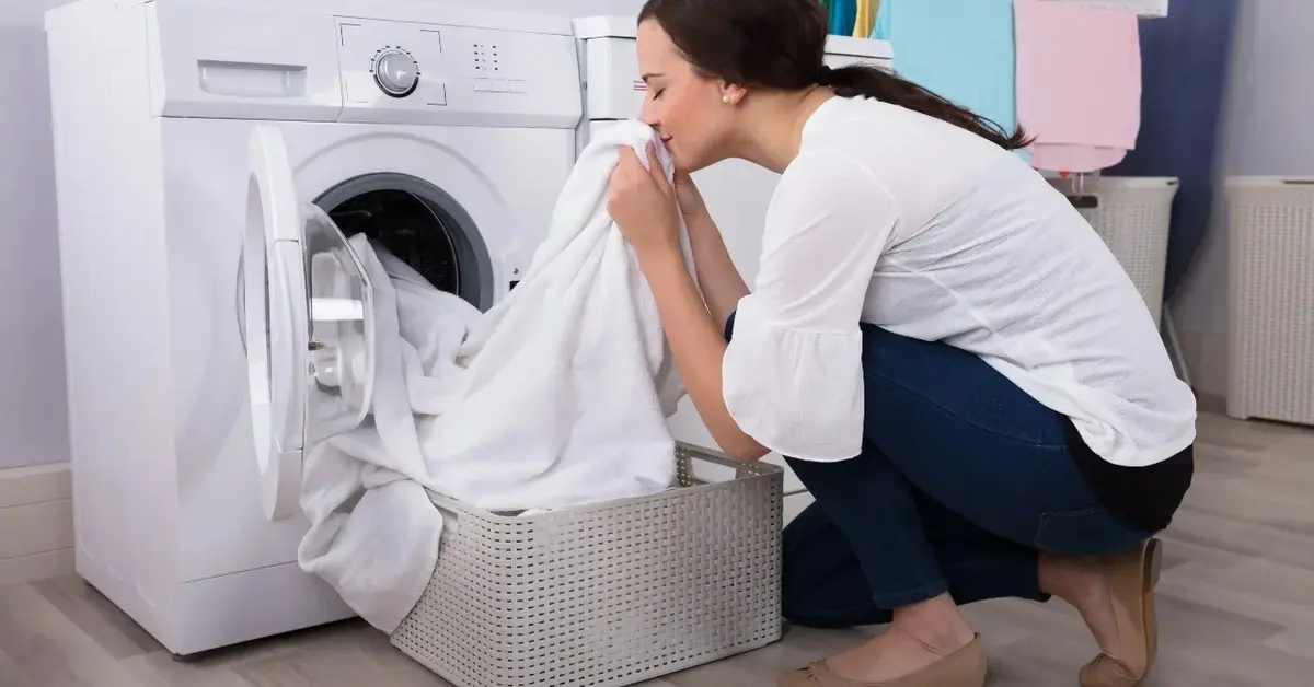Kobieta wyciągająca pranie z pralki i wąchająca je 