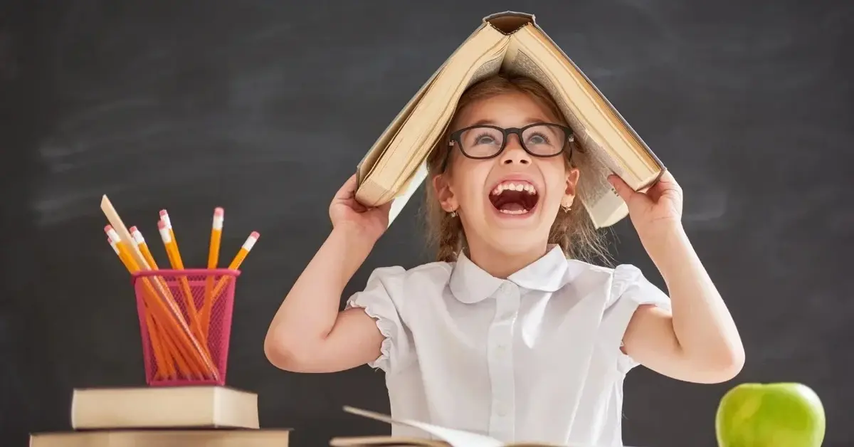 Dziecko przy biurku z przyborami szkolnymi z książką na głowie