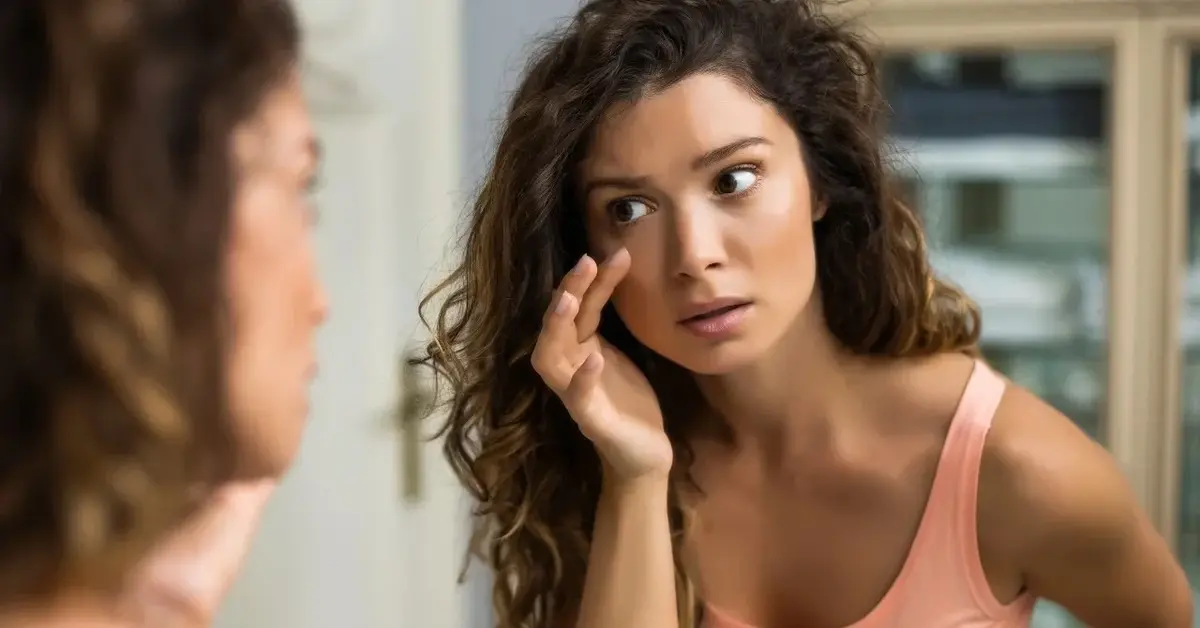 Kobieta przeglądająca się w lustrze dotykająca palcem skóry pod oczami 