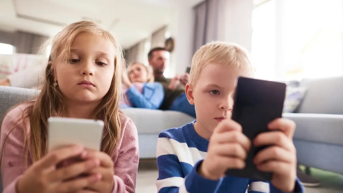Dziewczynka i chłopiec siedzący obok siebie i patrzący w swoje telefony