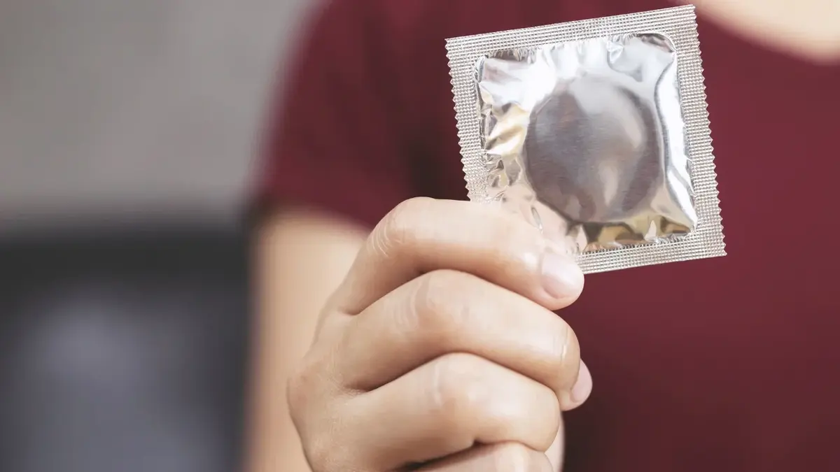 Kobieta trzymająca przed sobą prezerwatywę w opakowaniu 
