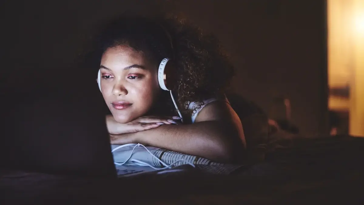 Kobieta elżąca na łóżku ze słuchawkami na uszach oglądająca coś na ekranie