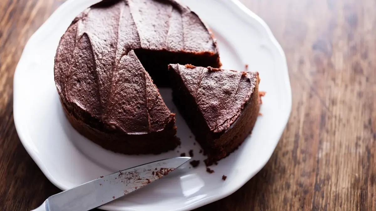 Ciasto czekoladowe na białym talerzy z wykrojonym i wysuniętym jednym trójkątnym kawałkiem.