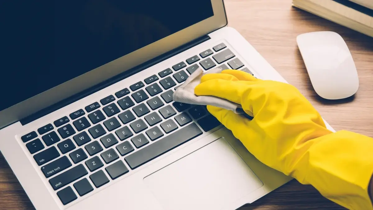 Ręka w żółtej rękawiczce wycierająca klawiature komputera