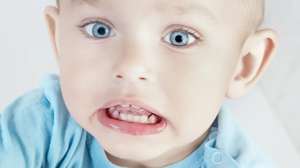 chłopiec w niebieskiej koszulce z niebieskimi oczami pokazuje zęby