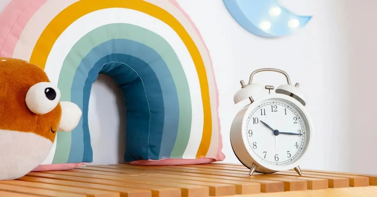 Zegar dla dzieci biały budzik przy dziecięcej ozdobie sówce i tęczy w pokoju dziecięcym