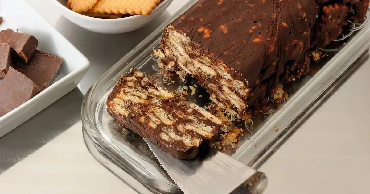 blok czekoladowy  na tacy ukrojony kawałek ze szpatułką z tylu herbatniki i kostki czekolady