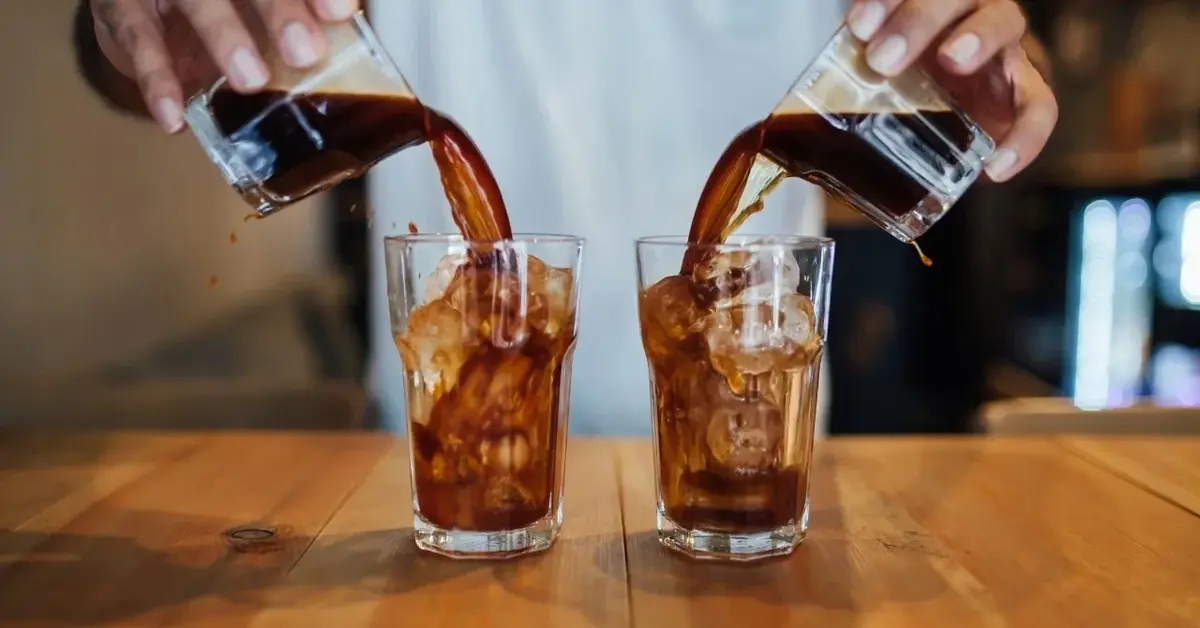 barista wlewa kawę do dwóch szklanek z lodem równocześnie