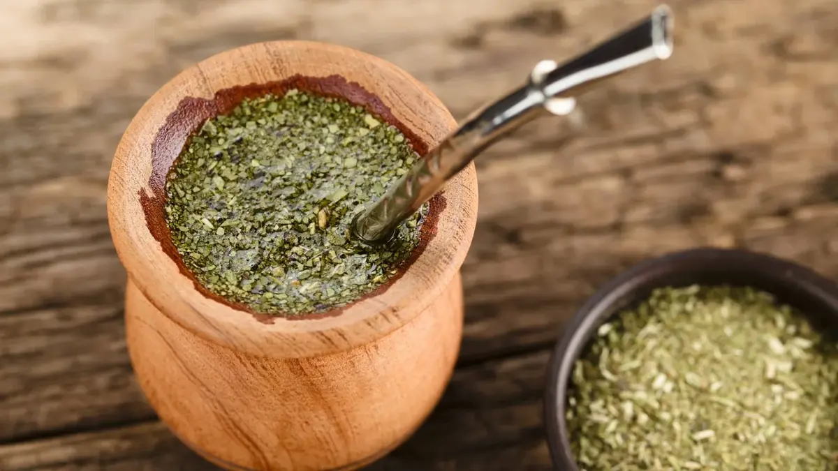 Yerba mate w naczyniu z metalową rurką, obok miseczka z suszoną Yerba mate