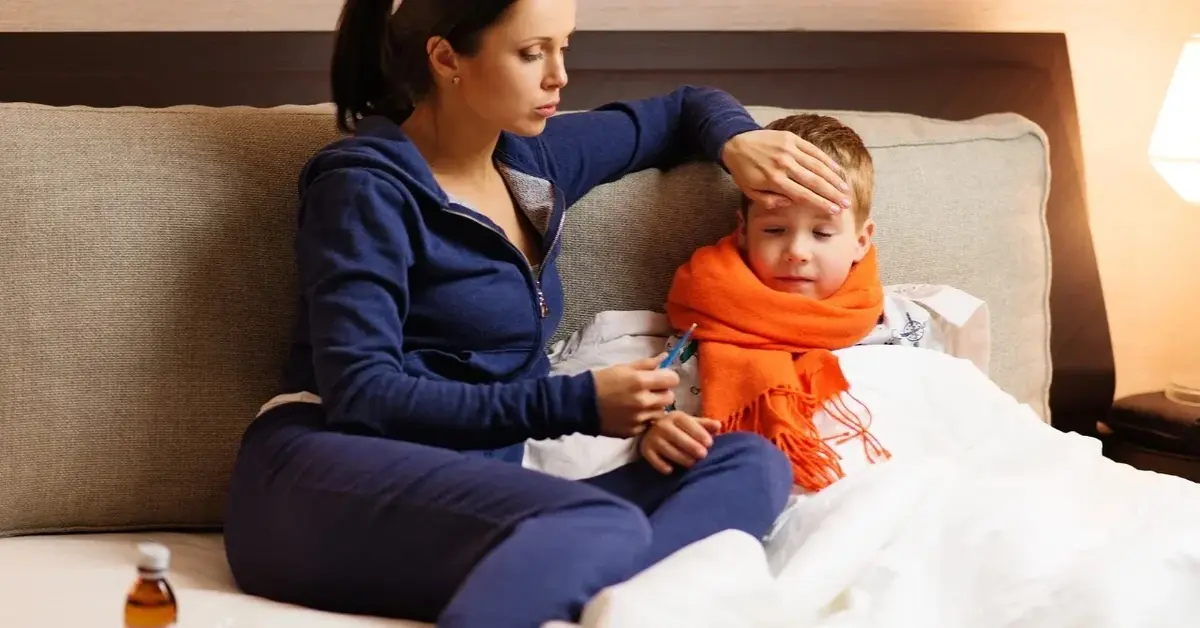 Mama sprawdzająca ręką temperaturę chłopca leżącego w lozku