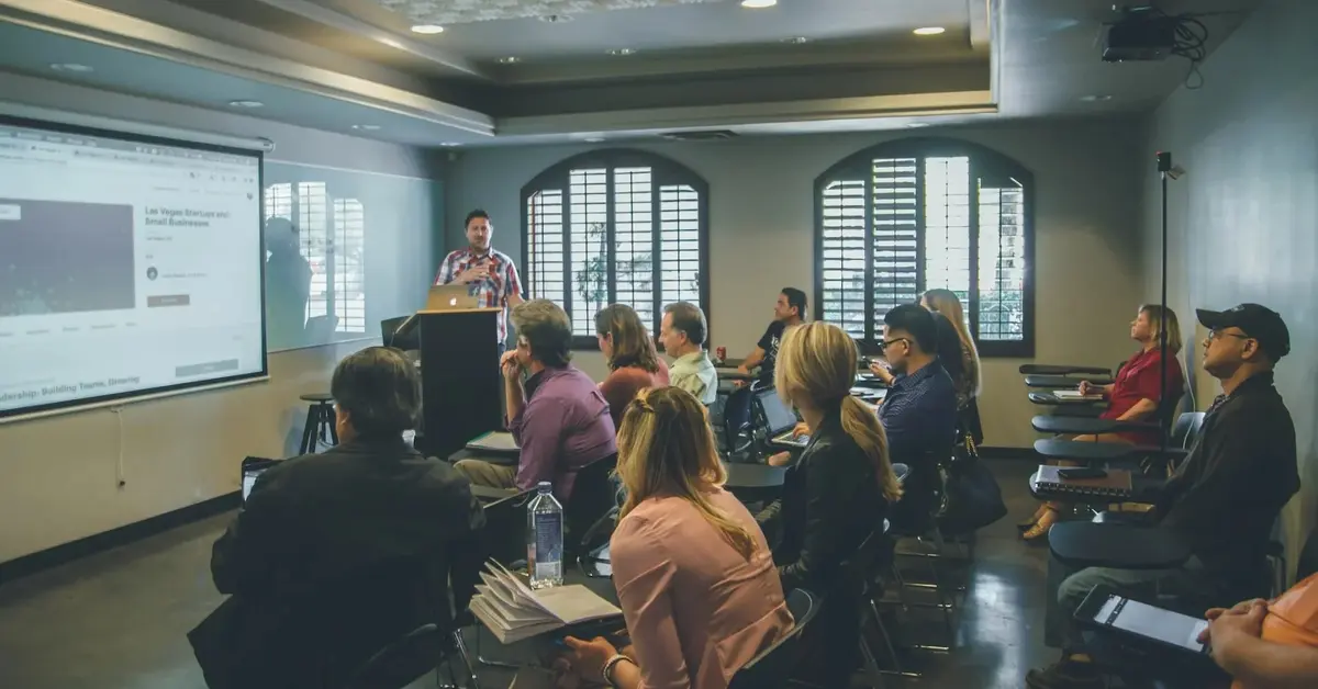 Sala wykładowa z multimedialną tablicą oraz łukowymi oknami pełna studentów szczęśliwych z wyboru studiów