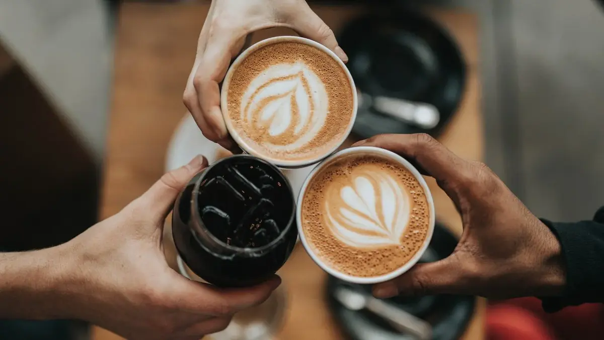 trzy kubki z kawą dwa cappucino i jedna z lodem trzymane w dłoniach 