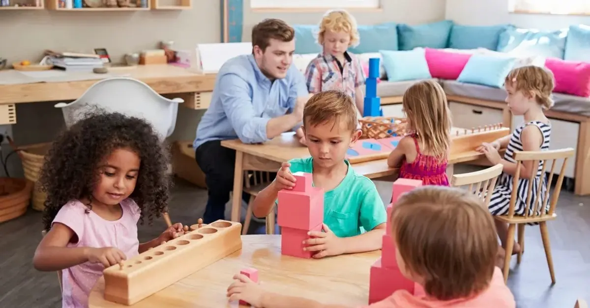 dzieci siedzą przy dwóch stolikach i zajmują się pracą nad pomocami montessori