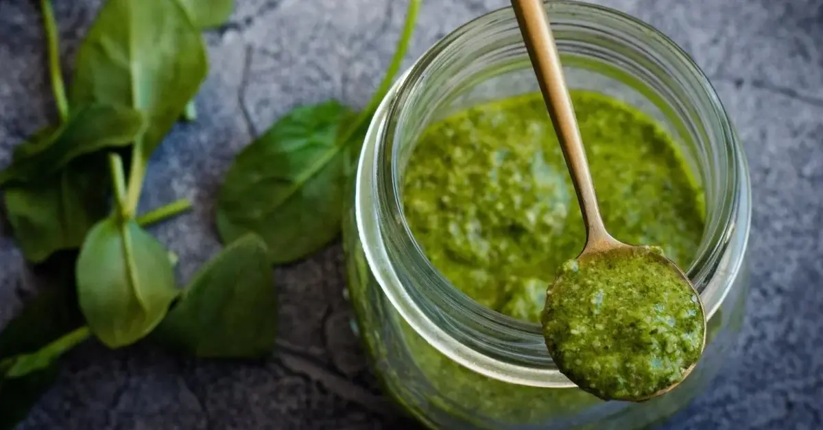 pesto bazyliowe  w słoiku na wierzchu łyżeczka z pesto obok listki bazylii