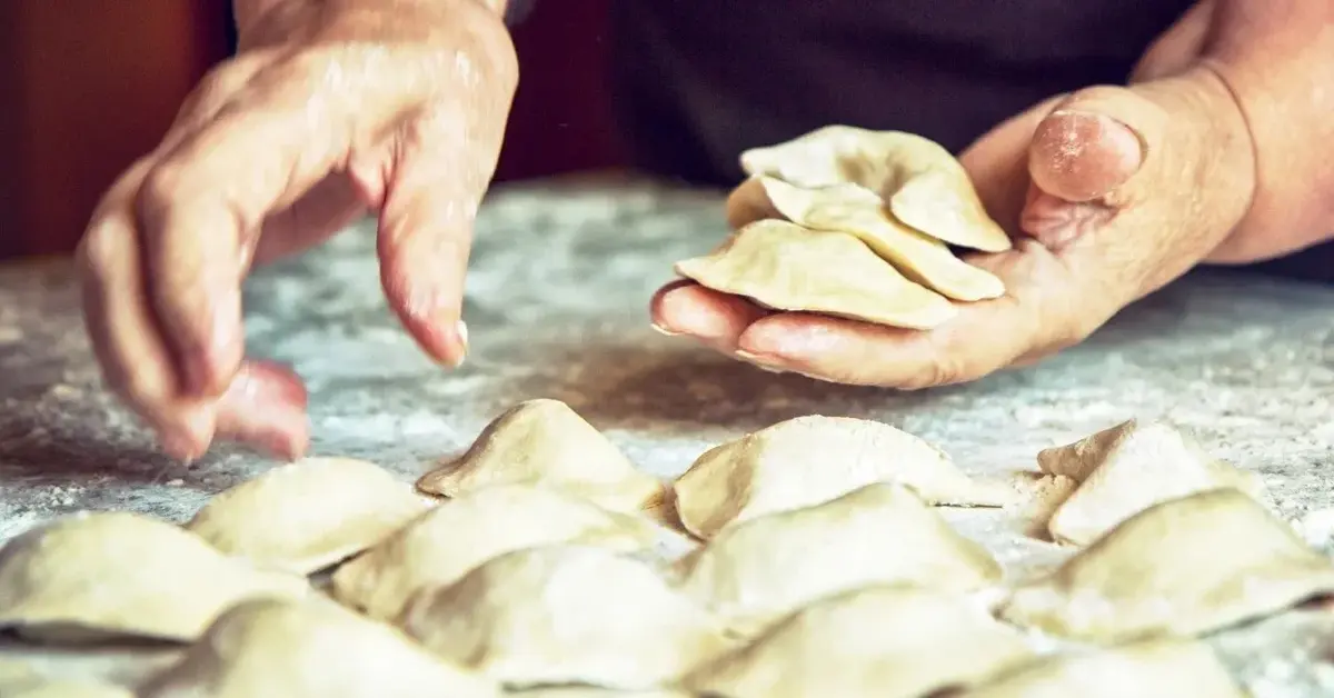 ręce podnoszą pierogi ze stolnicy