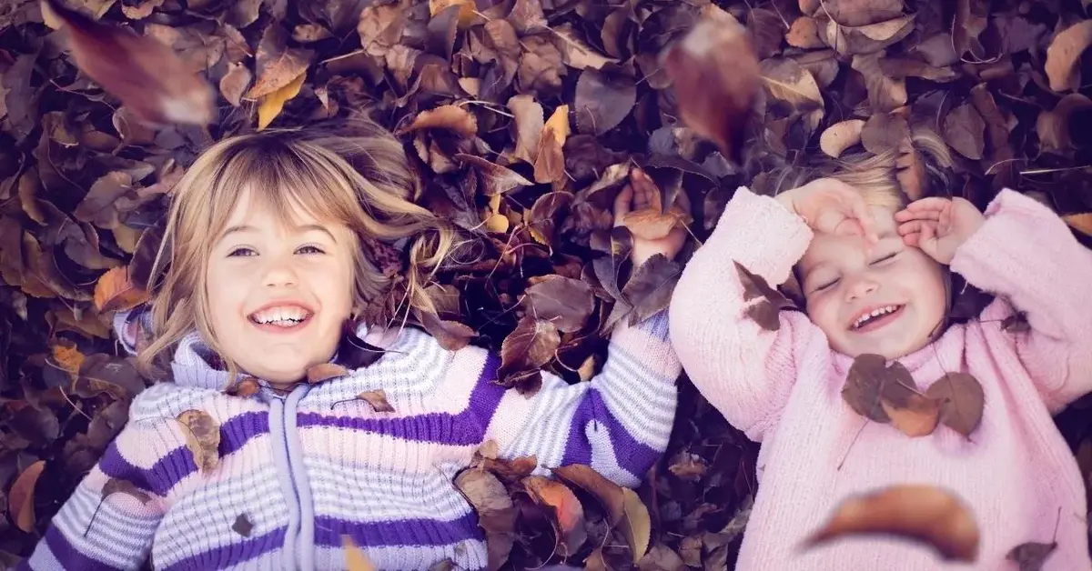Uśmiechnięte siostry leżą na jesiennych liściach.