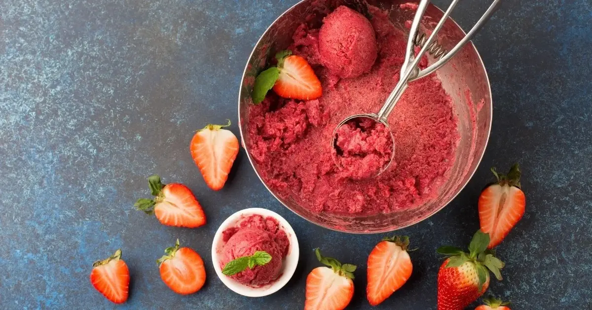 sorbet truskawkowy w misce z łyżką do lodów wokół połówki truskawek