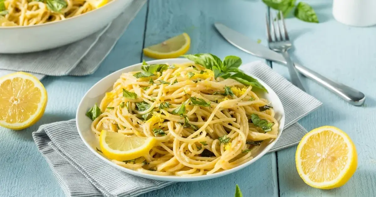 cytrynowe spaghetti na talerzu obok cytryny i sztućce