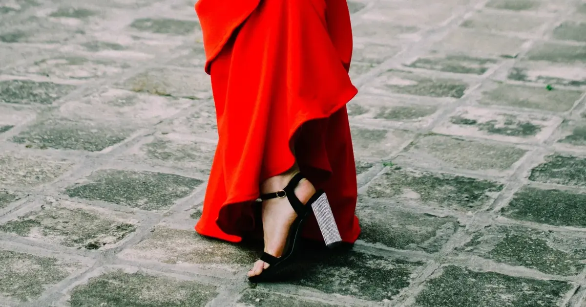 Piękna kobieta z włosami w kok prezentuje nogę w wysokim czarnym obcasie ubrana w czerwoną sukienkę wieczorową