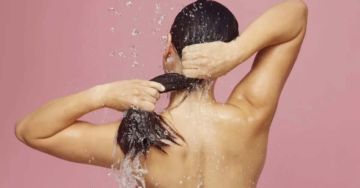 Kobieta z długimi czarnymi włosami pod prysznicem w trakcie mycia włosów