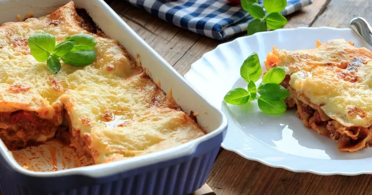 Lasagne w naczyniu do zapiekania i porcja na talerzu stojącym obok