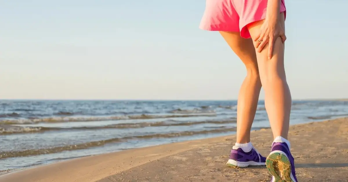 Kobieta w krótkich spodenkach na plaży trzymająca się za udo