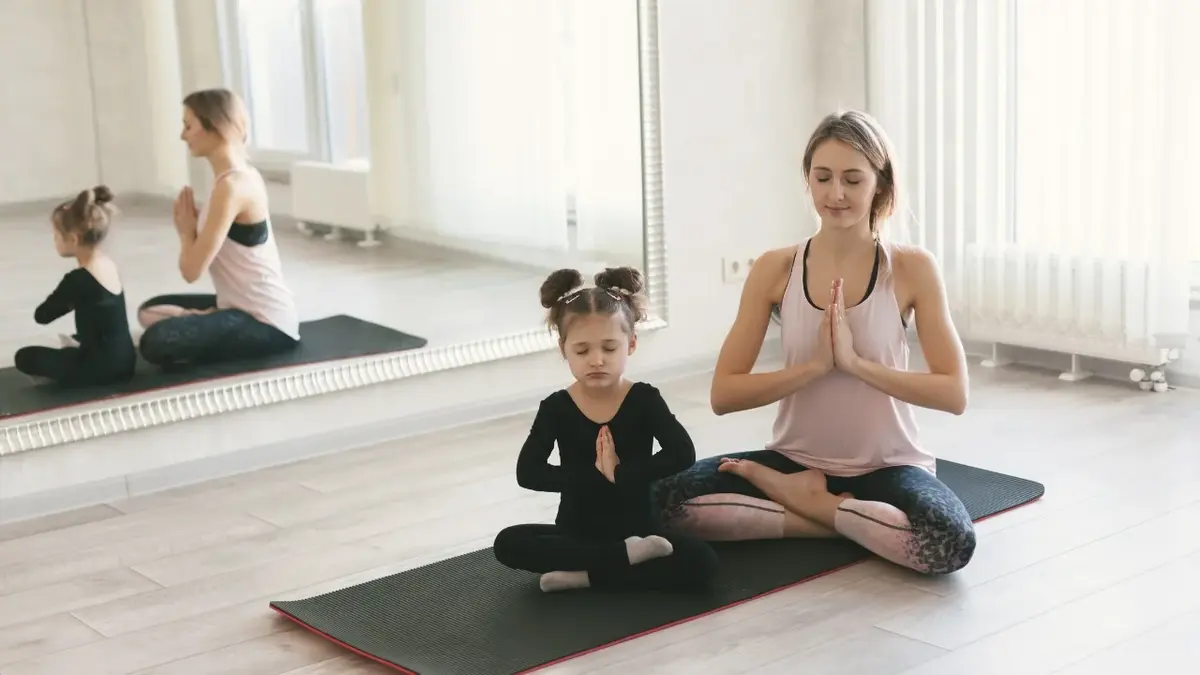 Mama i córka medytujące na macie w sali z lustrem 