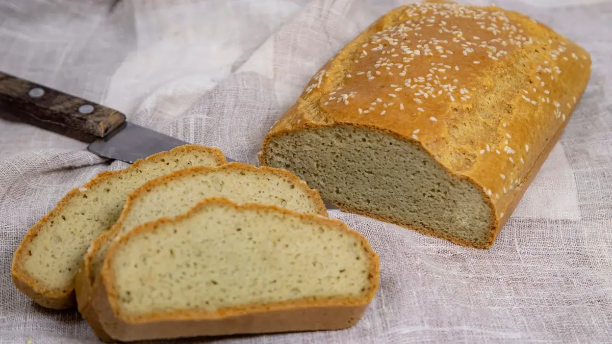 Chleb bezglutenowy, trzy kromki są pokrojone - w tle reszta bochenka
