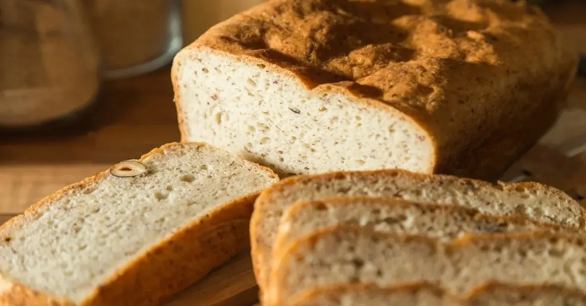 Chleb bezglutenowy, trzy kromki są pokrojone - w tle reszta bochenka